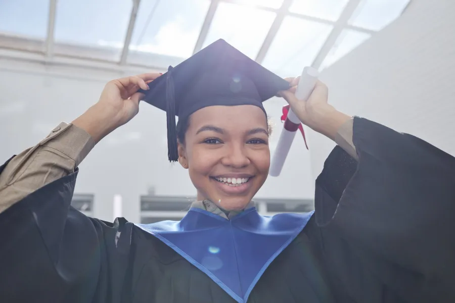 Smiling graduate in cap and gown holding a diploma
